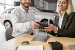 Female manager helps to male customer make payment for purchase of crossover.